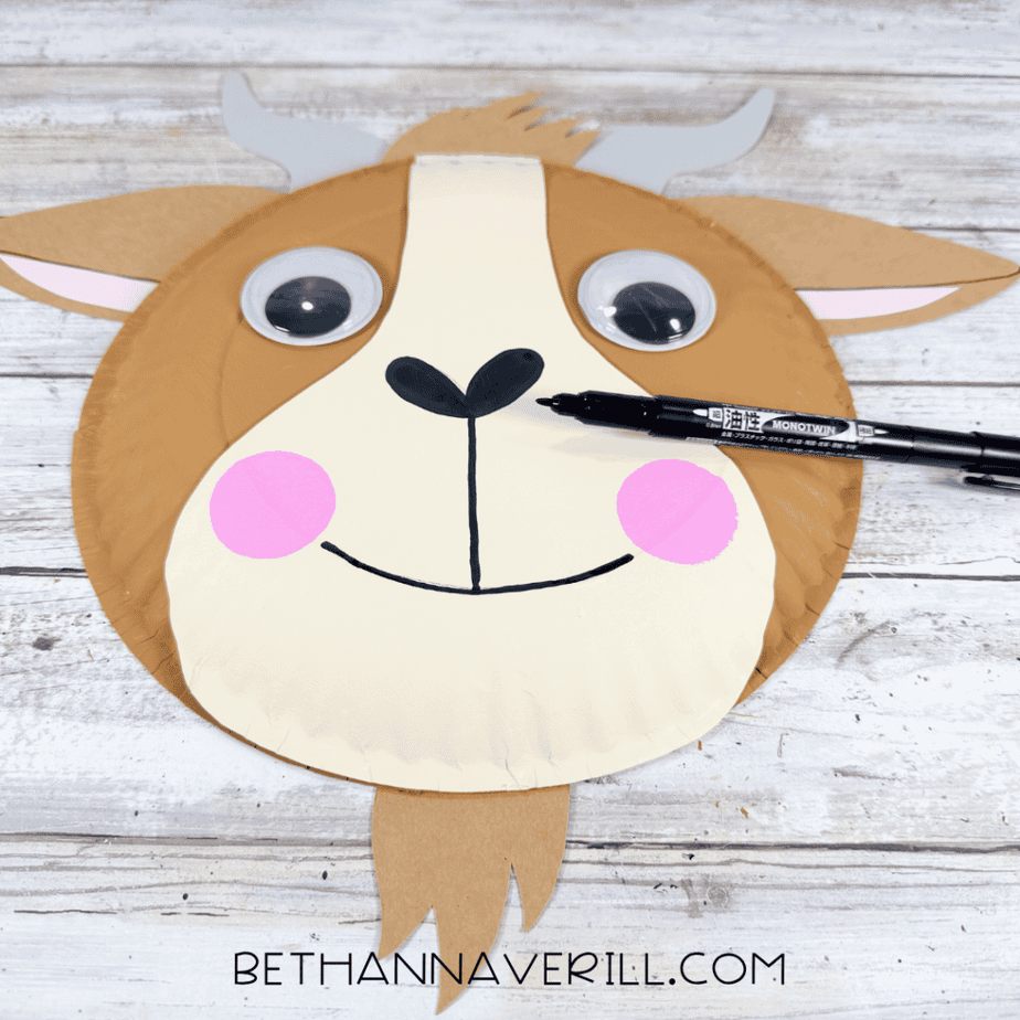 Paper plate animal face with pink cheeks and a black nose and smile, with a black marker resting across the face.