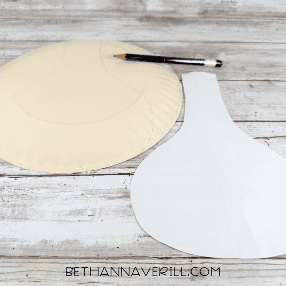 Cream-painted paper plate with curved pencil lines beside a white paper template and black pencil.