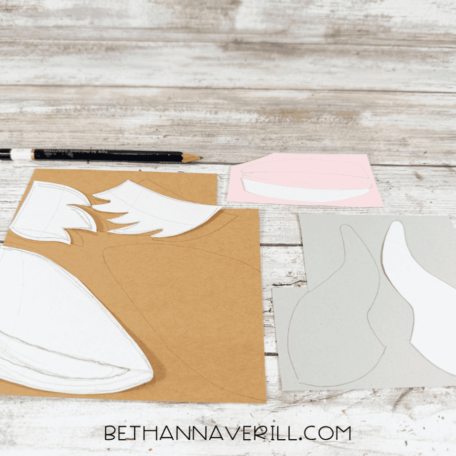 Paper templates and traced shapes arranged on brown, gray, and pink paper with a black pencil above them.