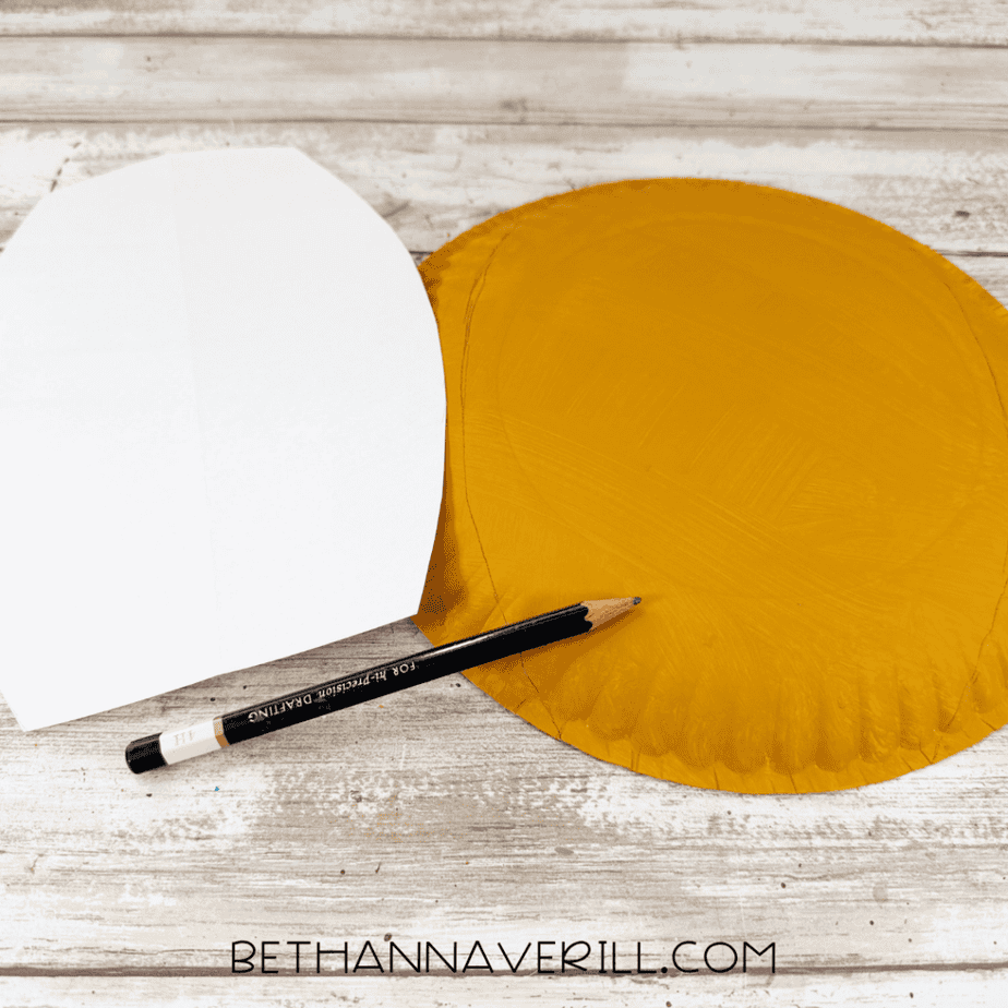 White paper template beside a golden yellow painted paper plate with pencil tracing lines around the plate.
