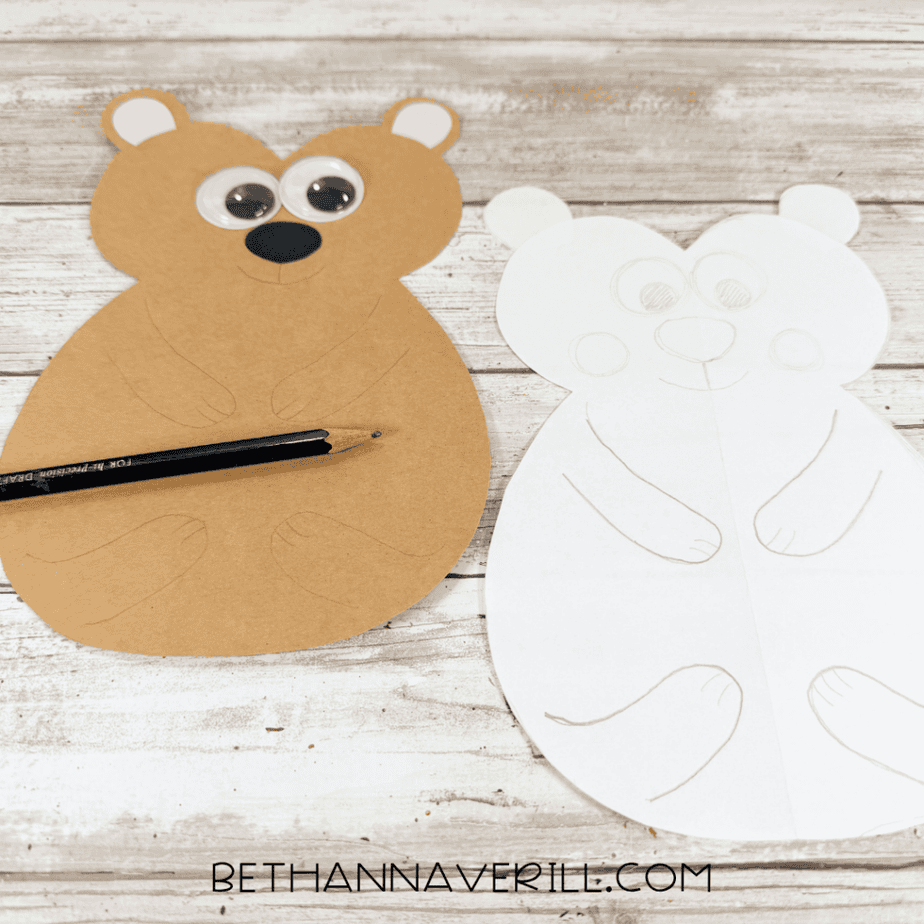 Tan paper animal shape with googly eyes, pink inner ears, black nose, and pencil-drawn facial and body details beside a white paper template.