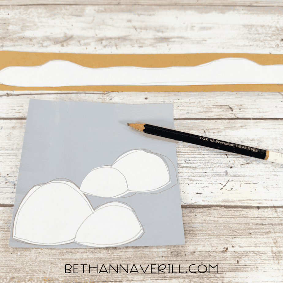White paper templates being traced onto gray and brown cardstock to create rock shapes and a long uneven strip.