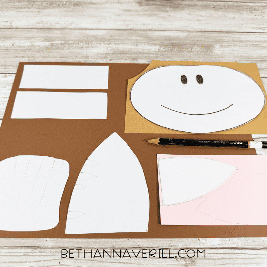 White paper templates arranged on brown, tan, and pink paper with traced outlines and a black pencil.
