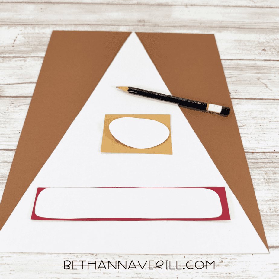 Brown, white, tan, and red paper pieces with templates arranged on a white wood surface beside a pencil.