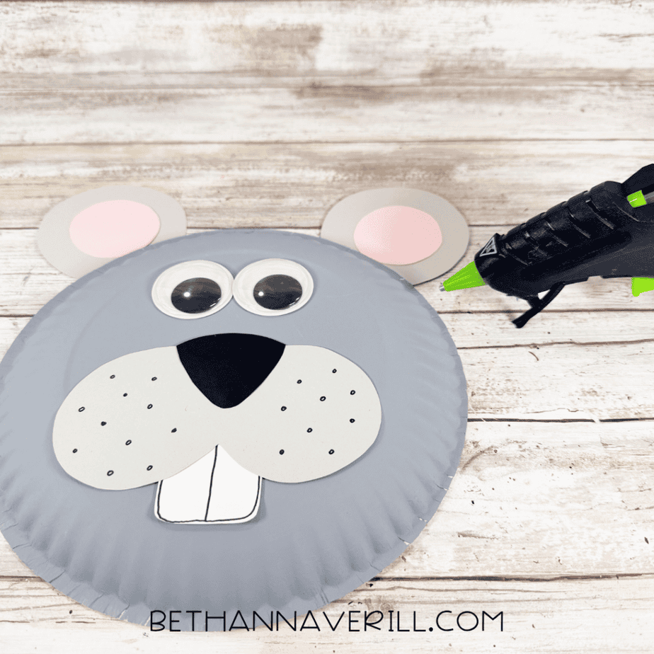 Gray paper plate mouse face with googly eyes, muzzle, nose, tooth, and two round gray ears with pink centers positioned at the top.