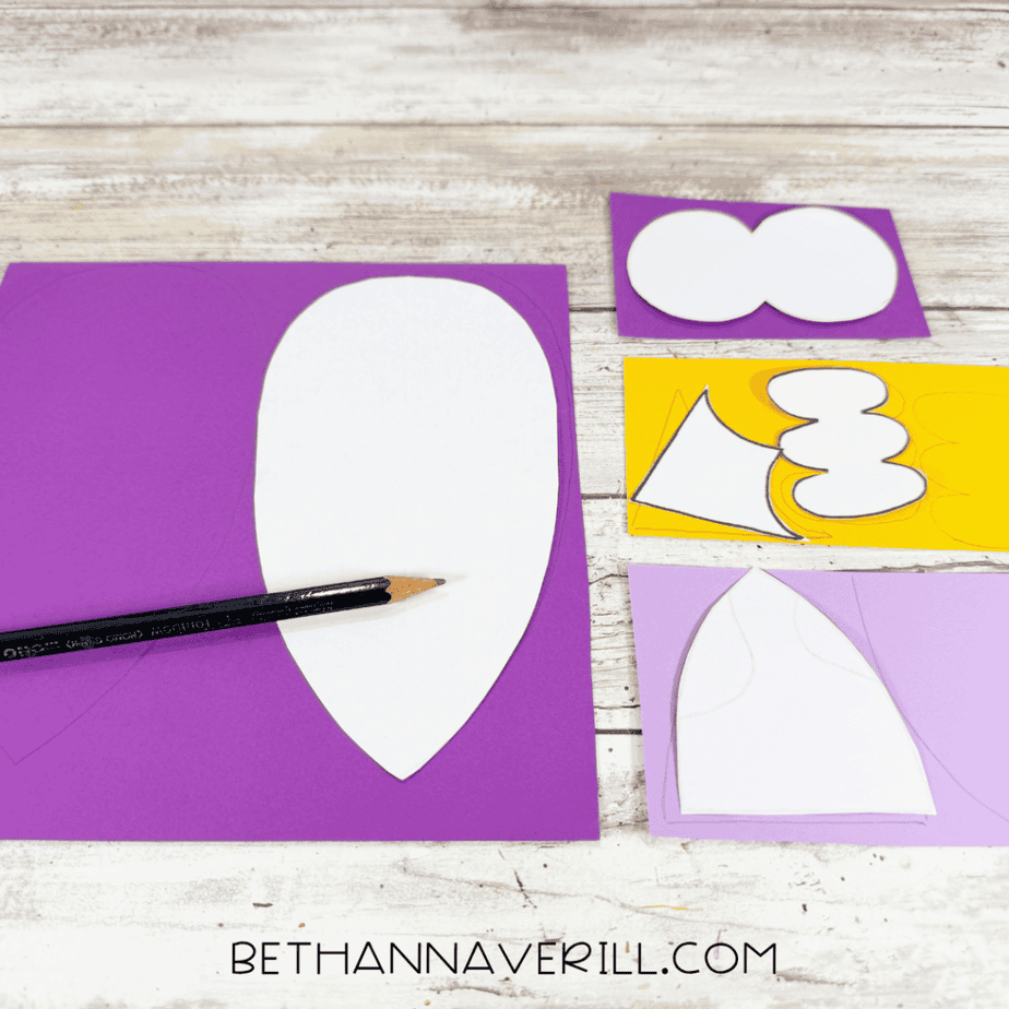 White paper templates arranged on purple, lavender, and yellow paper with traced outlines and a black pencil.