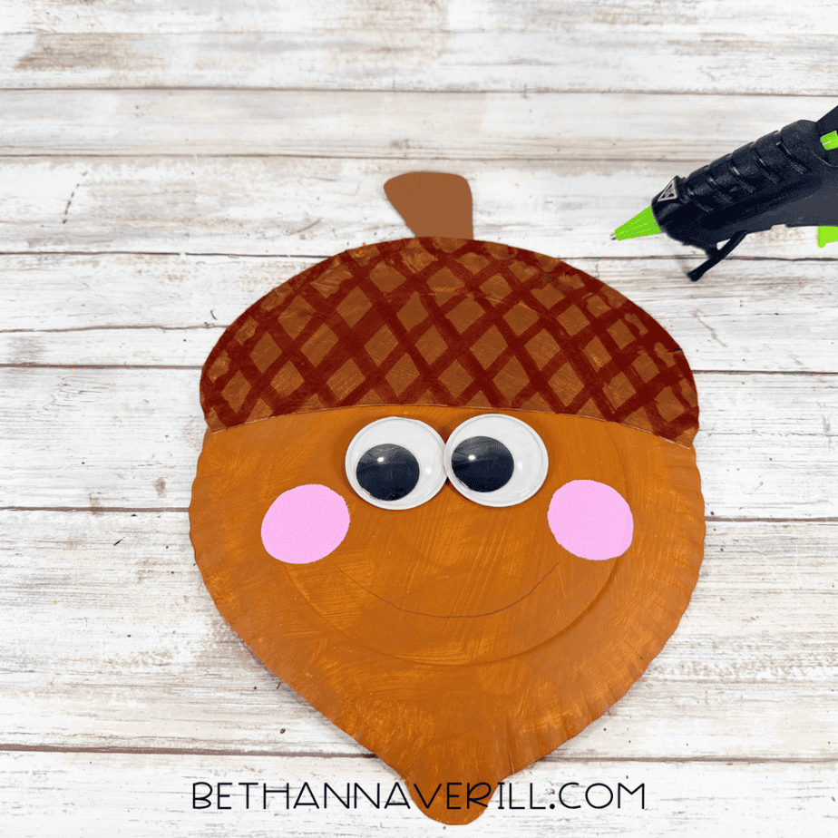 Brown paper stem attached to the top of an acorn paper plate craft using a hot glue gun.