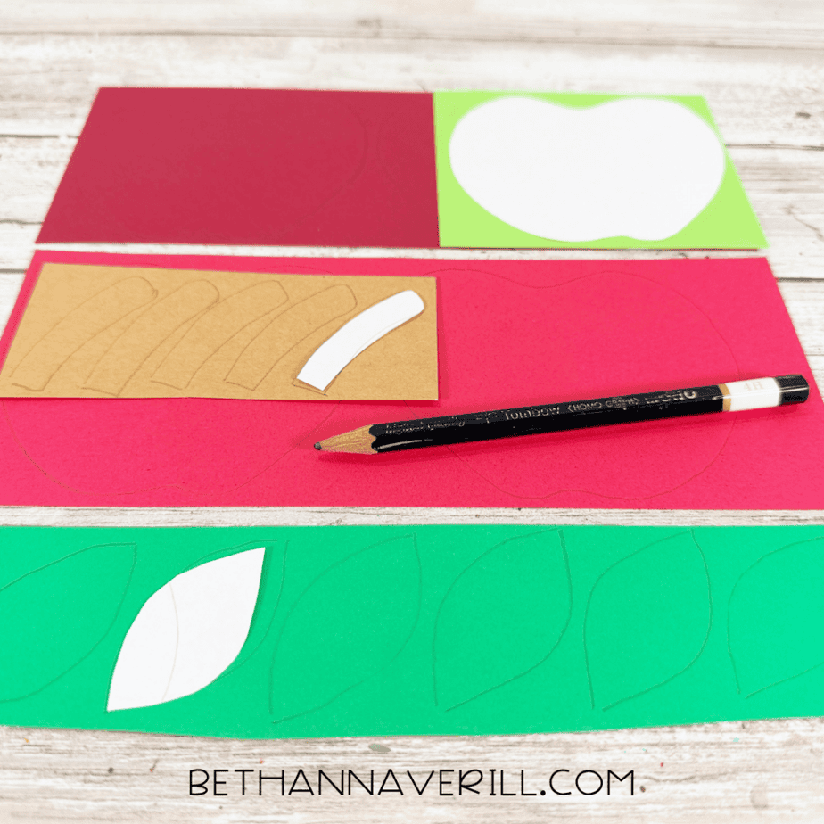 Apple, leaf, and stem templates traced onto red, green, and tan construction paper with a pencil.