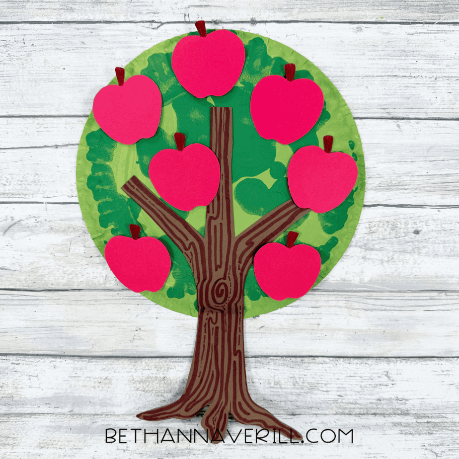 Finished apple tree paper plate craft featuring a green painted canopy, textured brown paper trunk, and seven bright red paper apples.