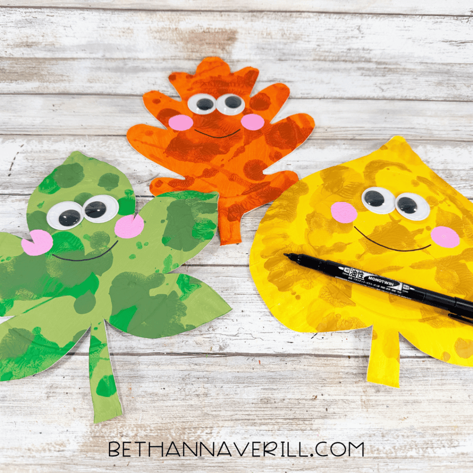 Black marker used to draw smiling faces on orange, yellow, and green autumn leaf paper plate crafts.