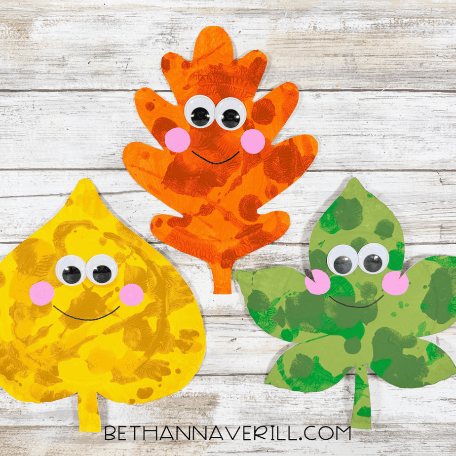 Finished autumn leaves paper plate crafts featuring three smiling leaves in orange, yellow, and green with googly eyes and pink cheeks.