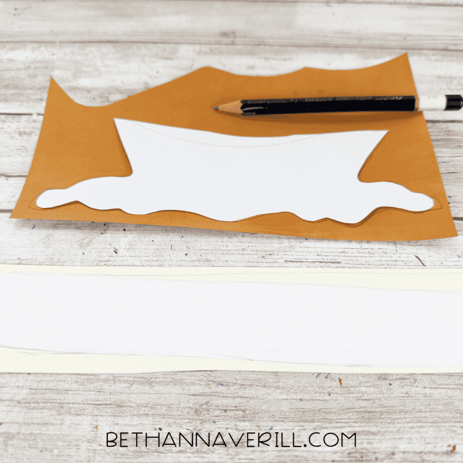 White paper template for a dripping caramel shape placed on brown cardstock with a pencil for tracing.