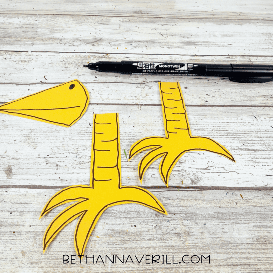 Yellow paper beak and two yellow bird legs outlined and detailed with a black marker.