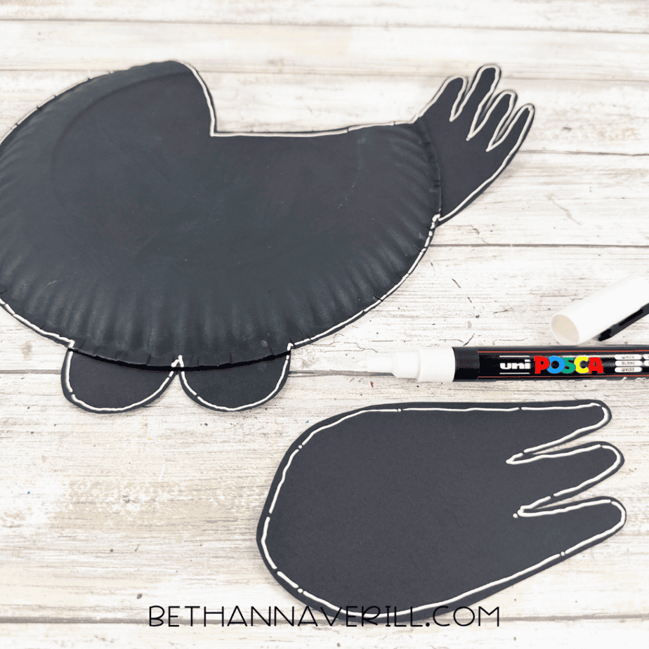 Black paper plate bird and separate black wing outlined with a white paint marker.