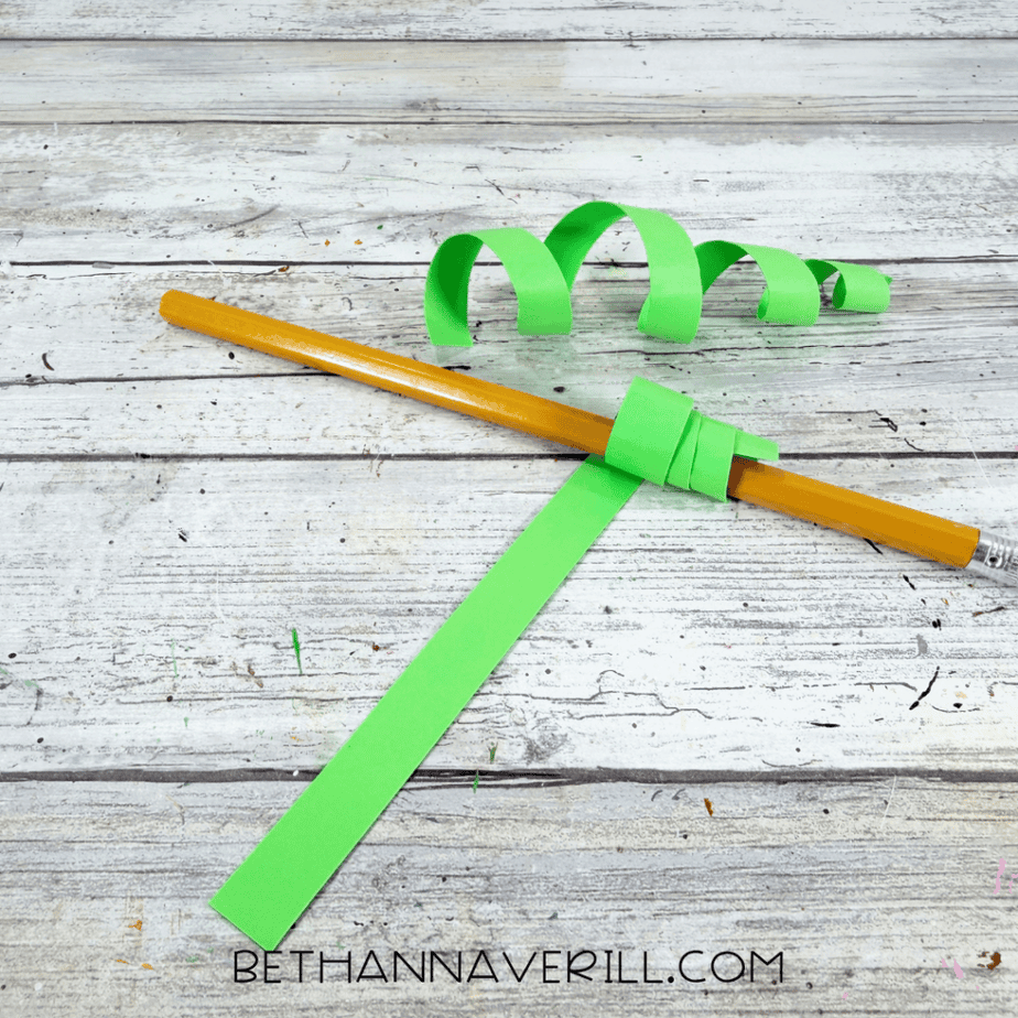 Long green paper strip wrapped around a pencil to form curled paper tendrils.