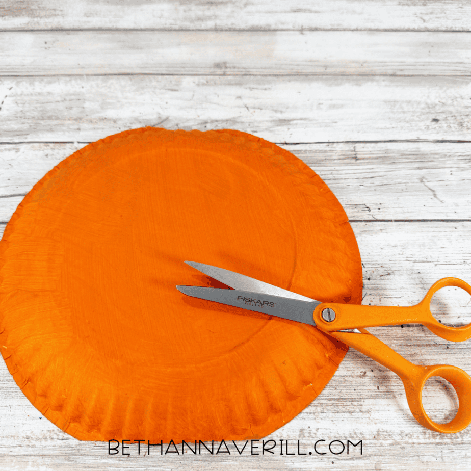 Orange painted paper plate with orange scissors resting over a curved pencil line.