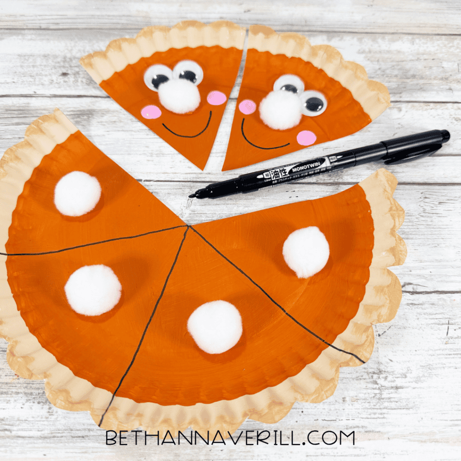 Pumpkin pie slices with smiling faces beside the remaining paper plate pie decorated with white pom poms.