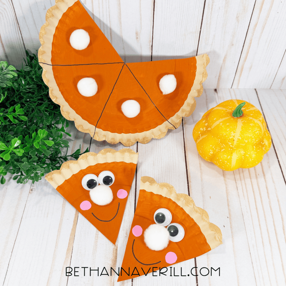 Finished pumpkin pie paper plate craft with two smiling pie slices displayed beside the remaining pie and a small decorative pumpkin.