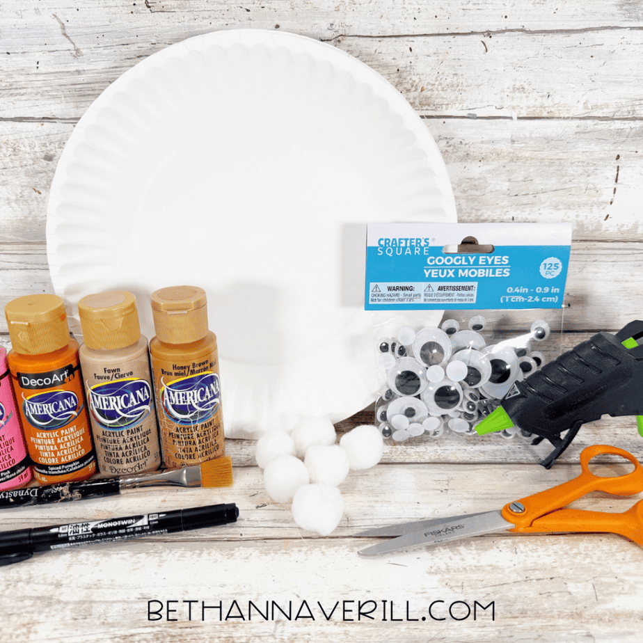 Supplies for a pumpkin pie paper plate craft including paper plates, acrylic paint, googly eyes, white pom poms, scissors, markers, paintbrushes, and a hot glue gun.
