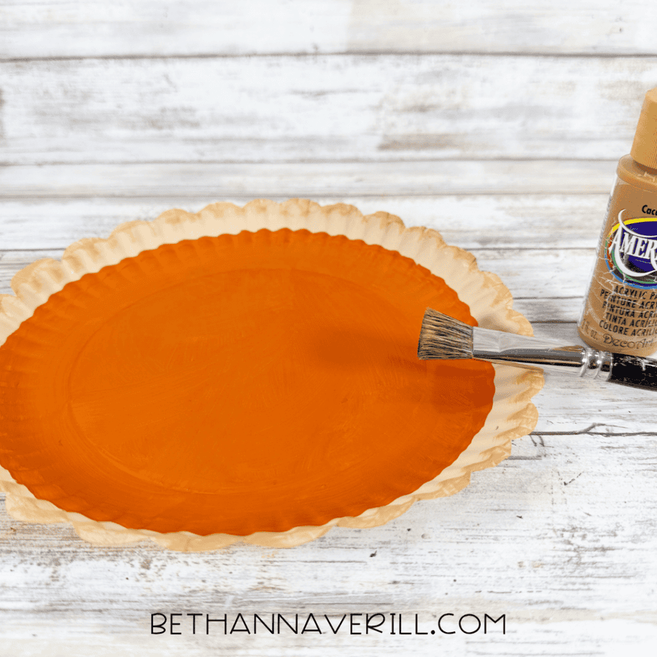 Orange paper plate with the outer rim painted tan to resemble a pumpkin pie crust.