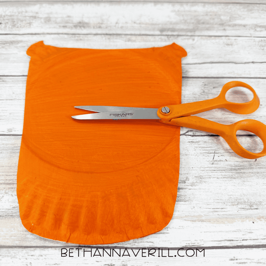 Orange painted paper plate trimmed into a rounded cup shape with orange scissors resting on top.